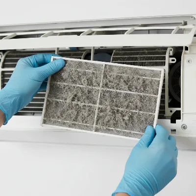 Hands cleaning a dirty air filter inside an air conditioner unit to reduce noise